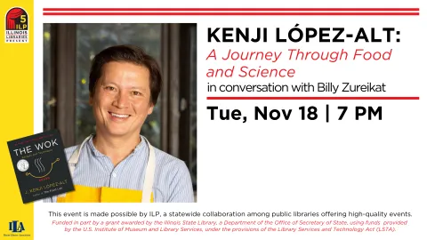 Kenji Lopez smiles at the camera. He is wearing a white button-up shirt with blue stripes and a bright yellow apron. 