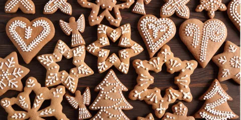 Gingerbread cookies of various shapes are arranged on a wooden table. The shapes include hearts, snowflakes, and Christmas trees. 