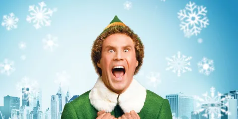 Buddy from the film "Elf" wears a wide-mouthed expression of joy. A pointed green hat with gold details sits above his head. A tight suit with a fluffy white collar adorns his body. His hands are held in fists at his chest, betraying a barely contained excitement. Behind him is a blue sky and the silhouettes of even bluer buildings beneath it. Snowflakes of varying sizes float throughout the scene. 