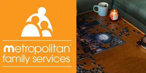The metropolitan family services logo - which is a bright orange background with several huddled abstract figures. On the right there is a wooden table with a puzzle and a coffee mug on top. 