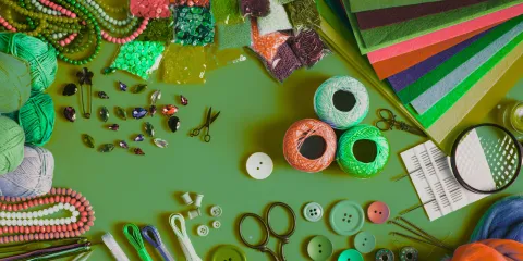 A bright green table filled with crafting supplies, including: scissors, pipe cleaners, and thread. 
